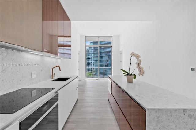 kitchen featuring sink, tasteful backsplash, a wall of windows, wall oven, and white cabinets