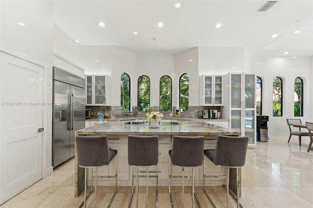 kitchen featuring light stone countertops, tasteful backsplash, white cabinets, and built in fridge