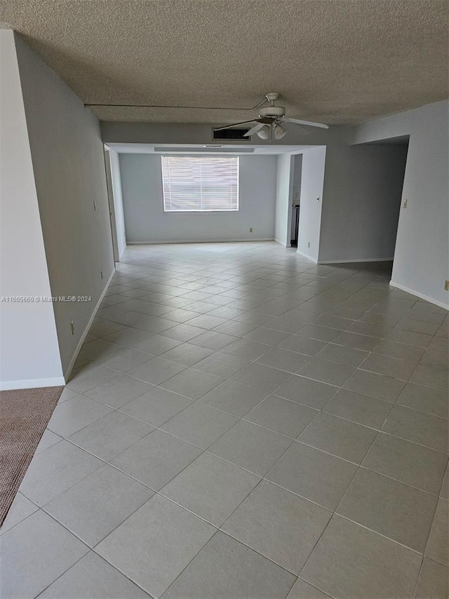 tiled empty room featuring baseboards, a textured ceiling, and a ceiling fan