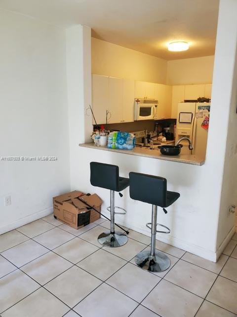 kitchen with refrigerator with ice dispenser, kitchen peninsula, and light tile patterned floors