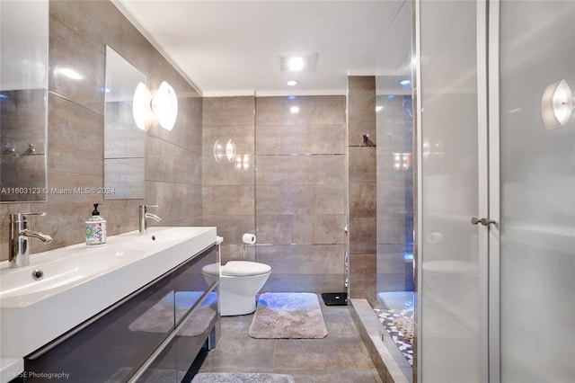 bathroom with toilet, tile walls, tiled shower, vanity, and tile patterned flooring