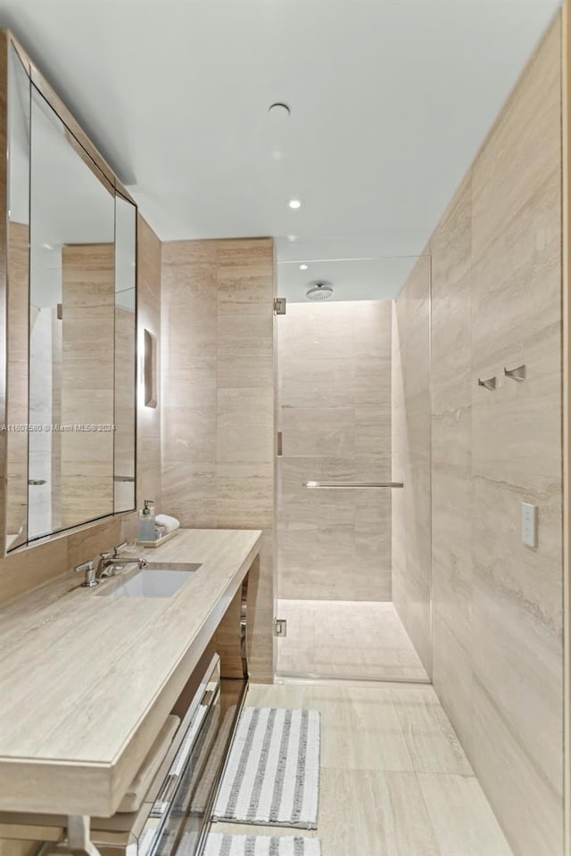 bathroom featuring a shower with door, vanity, and tile walls