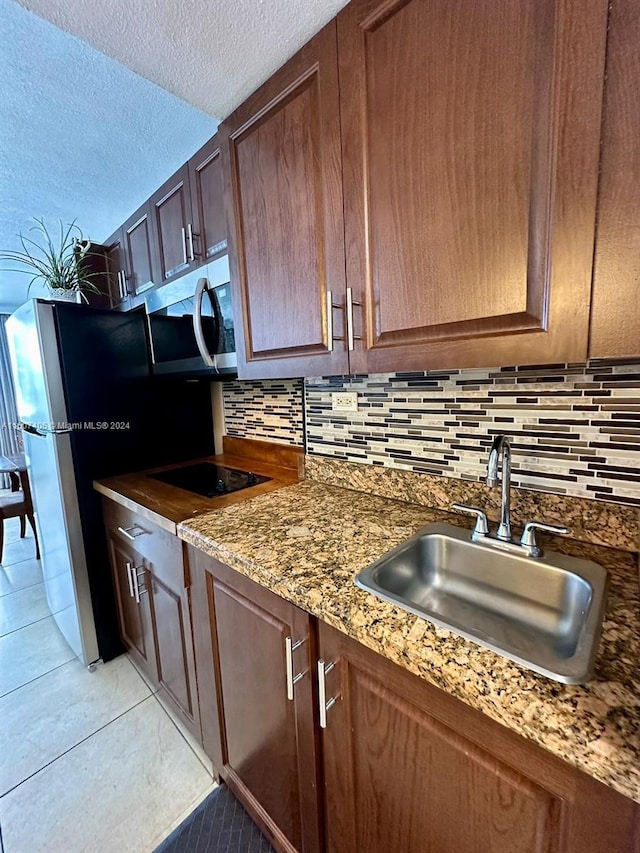 kitchen featuring stainless steel appliances, sink, light tile patterned flooring, tasteful backsplash, and a textured ceiling