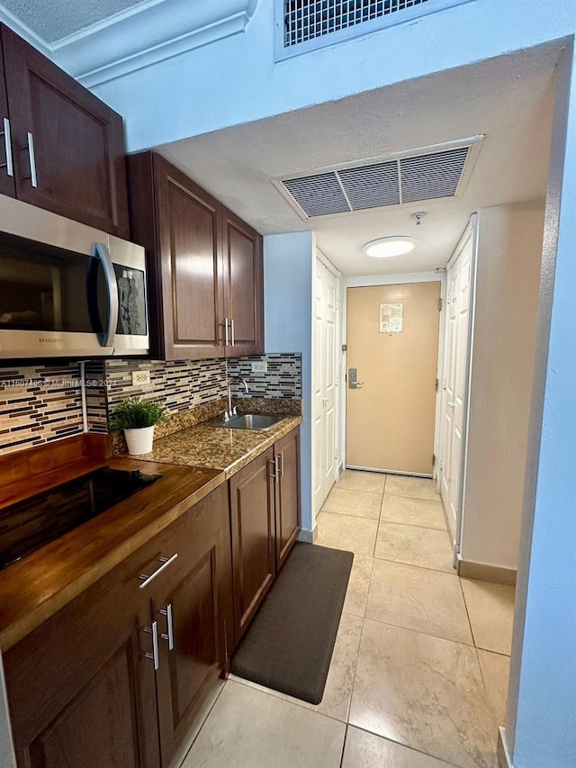 kitchen featuring light tile patterned floors, sink, dark stone counters, decorative backsplash, and dark brown cabinetry