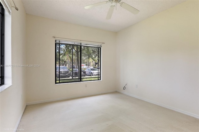 empty room featuring ceiling fan, light colored carpet, and a textured ceiling