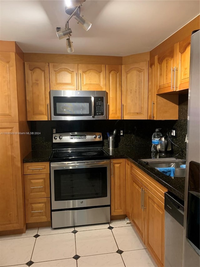 kitchen featuring dark stone countertops, stainless steel appliances, backsplash, rail lighting, and light tile flooring