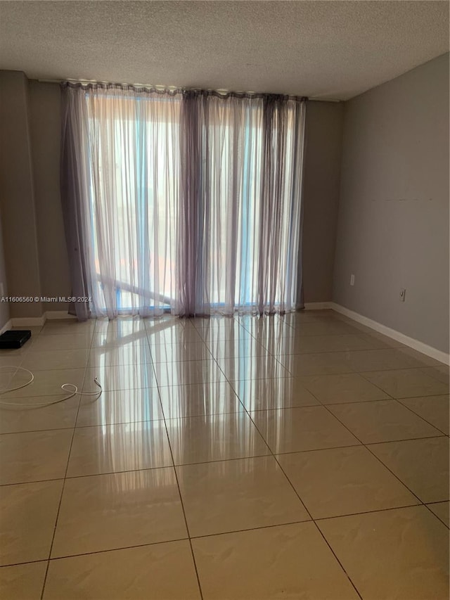 empty room with tile floors, plenty of natural light, and a textured ceiling