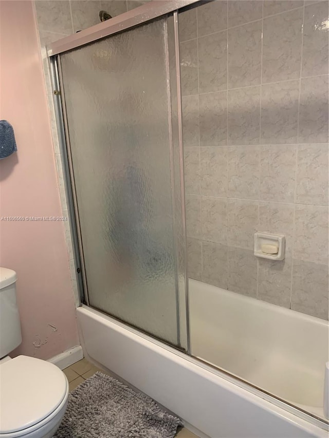 bathroom featuring tile floors, shower / bath combination with glass door, and toilet