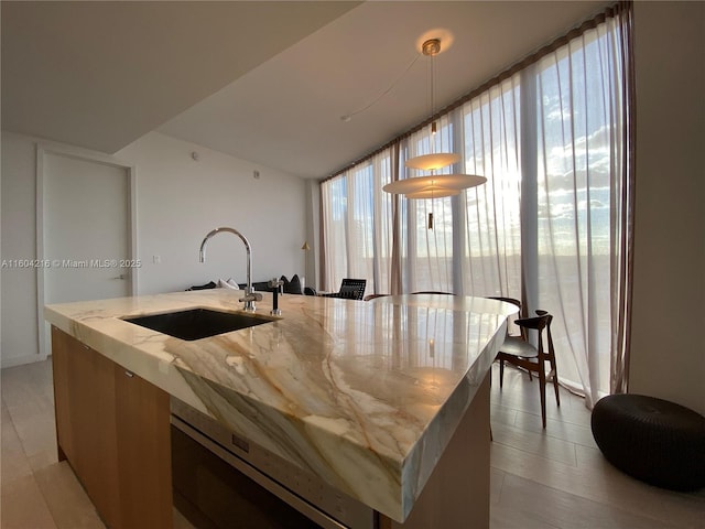 kitchen featuring an island with sink, expansive windows, a sink, and hanging light fixtures