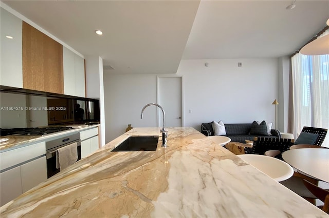 kitchen featuring stainless steel appliances, a sink, white cabinets, light stone countertops, and modern cabinets