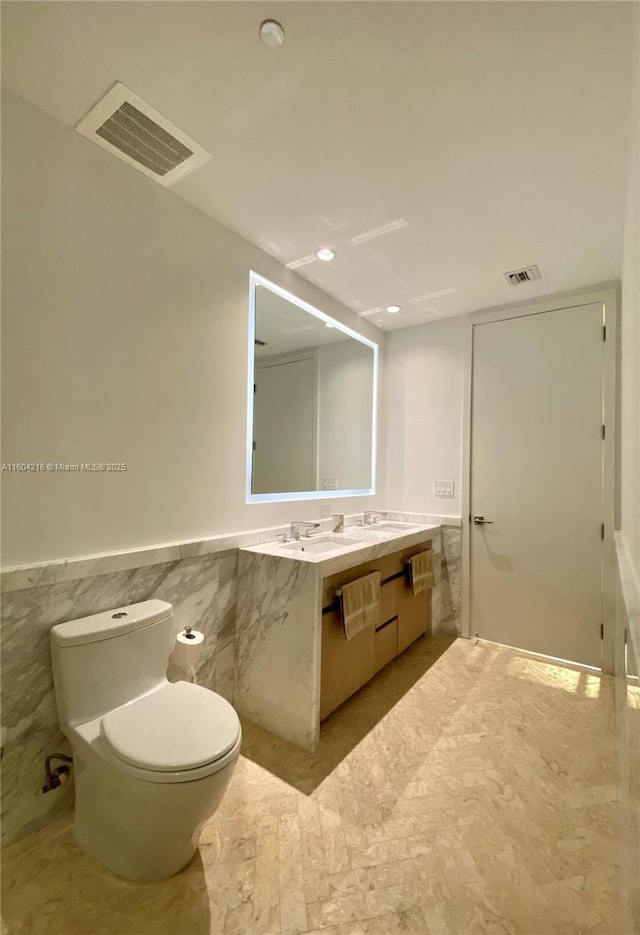 bathroom with double vanity, visible vents, tile walls, and wainscoting