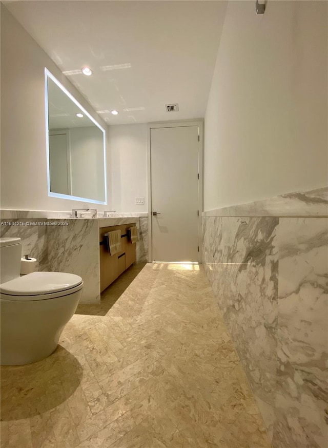 bathroom with toilet, wainscoting, tile walls, and vanity