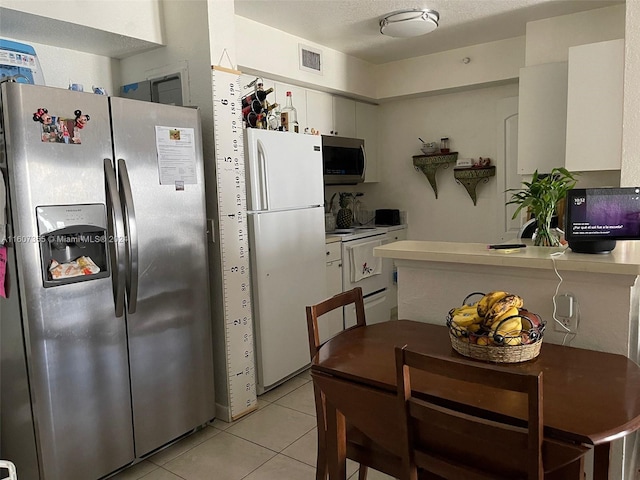 kitchen featuring a textured ceiling, white cabinets, light tile patterned floors, and appliances with stainless steel finishes