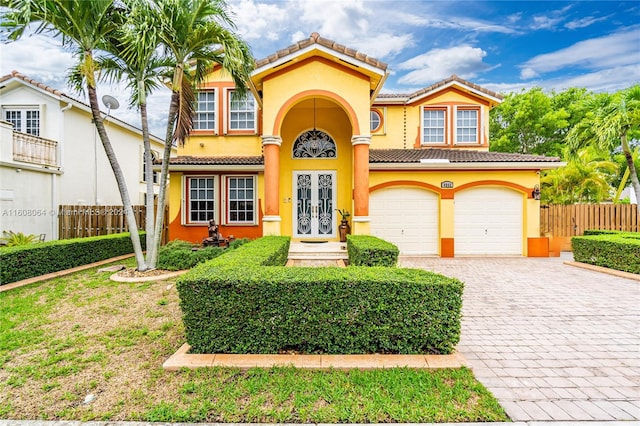 mediterranean / spanish-style home featuring decorative driveway, a tile roof, stucco siding, an attached garage, and fence