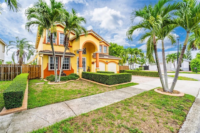 mediterranean / spanish home with a tile roof, stucco siding, a front yard, fence, and driveway