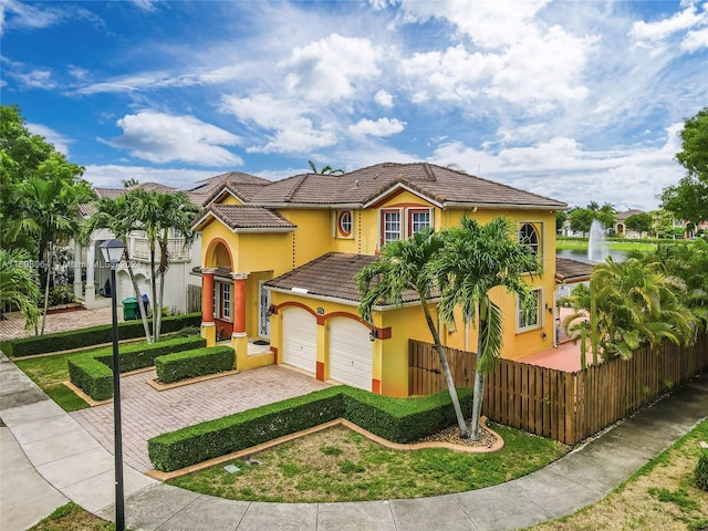 mediterranean / spanish house with decorative driveway, a tile roof, fence, and stucco siding