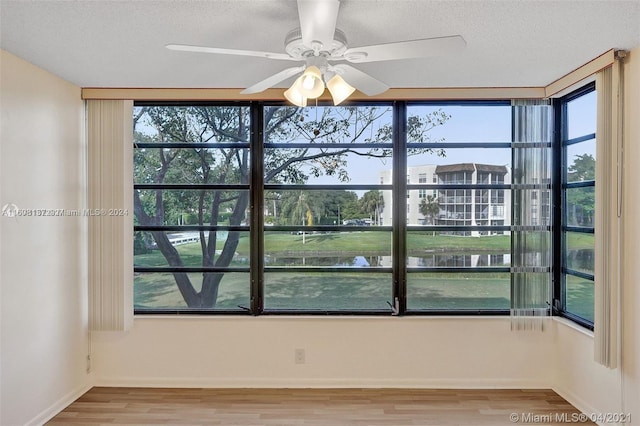 empty room featuring ceiling fan, hardwood / wood-style floors, a water view, and a textured ceiling