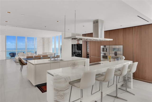 kitchen with a spacious island, white cabinets, island exhaust hood, a wall of windows, and sink