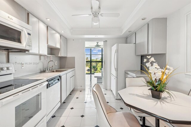 kitchen with ceiling fan, a tray ceiling, sink, white appliances, and light tile floors