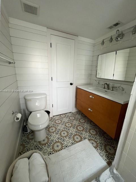 bathroom with tile patterned flooring, vanity, toilet, and wooden walls