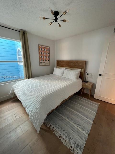 bedroom with ceiling fan with notable chandelier, wood-type flooring, and a textured ceiling