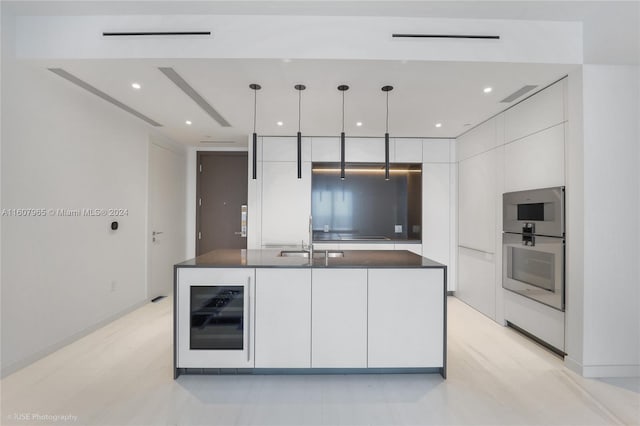 kitchen with beverage cooler, an island with sink, decorative light fixtures, sink, and white cabinetry