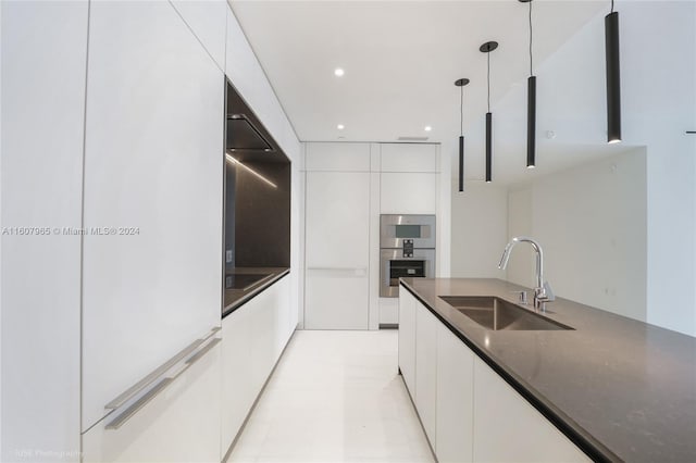 kitchen featuring dark stone counters, light tile floors, hanging light fixtures, sink, and white cabinetry