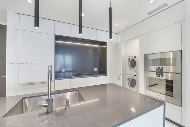 kitchen with dark stone counters, stacked washer / drying machine, stainless steel double oven, and white cabinets