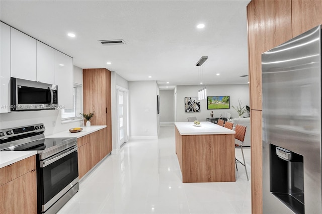 kitchen featuring stainless steel appliances, a kitchen island, light tile patterned floors, decorative light fixtures, and white cabinetry