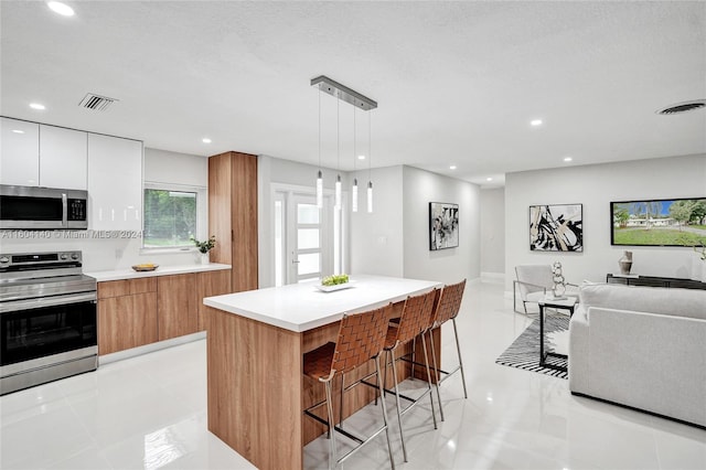 kitchen featuring pendant lighting, white cabinets, a breakfast bar area, a kitchen island, and stainless steel appliances