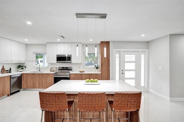 kitchen with a center island, white cabinets, sink, appliances with stainless steel finishes, and decorative light fixtures