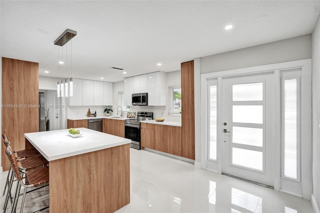 kitchen with pendant lighting, a center island, a kitchen breakfast bar, appliances with stainless steel finishes, and white cabinetry