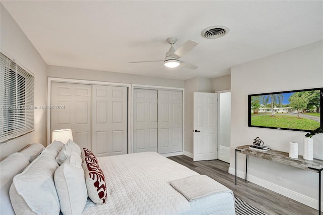 bedroom with ceiling fan, dark hardwood / wood-style floors, and two closets