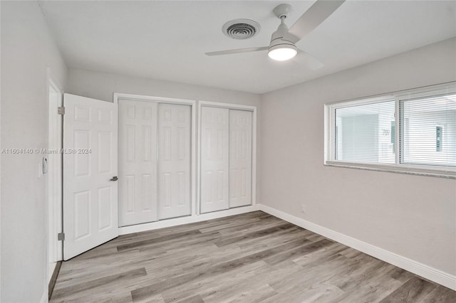 unfurnished bedroom featuring ceiling fan, light wood-type flooring, and two closets