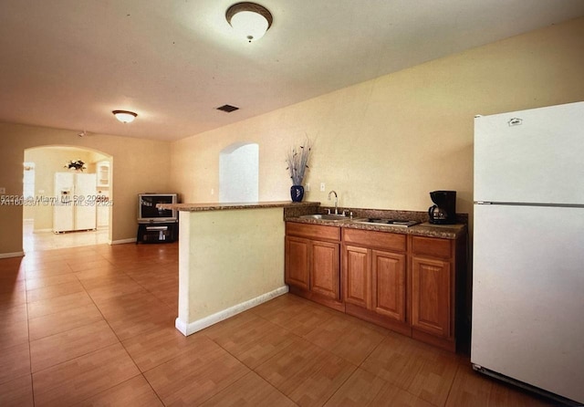 kitchen featuring kitchen peninsula, white fridge, stainless steel gas stovetop, and sink