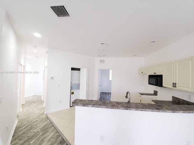 kitchen with stacked washer / dryer, kitchen peninsula, light tile patterned flooring, and sink