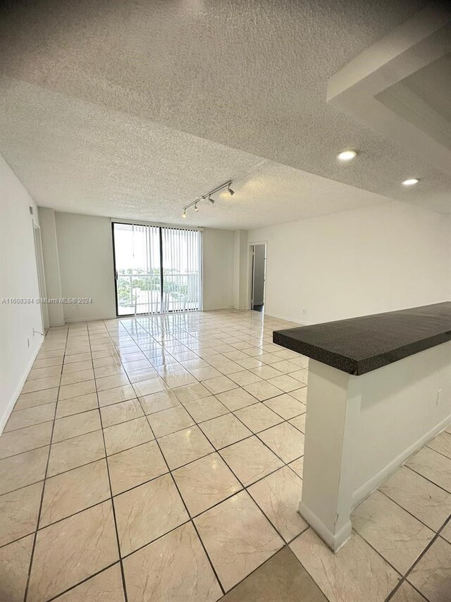 tiled spare room featuring a textured ceiling, expansive windows, and rail lighting