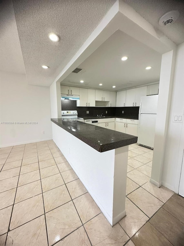 kitchen with light tile patterned flooring, a textured ceiling, kitchen peninsula, white appliances, and white cabinets