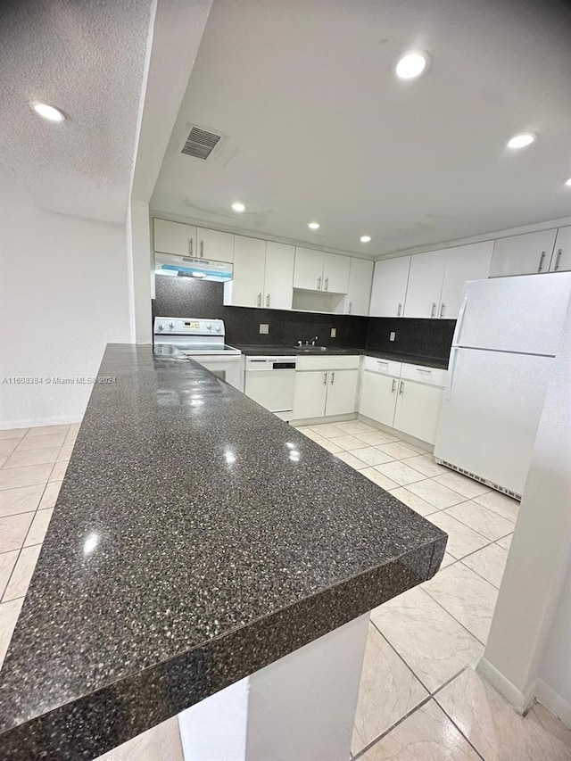 kitchen with a textured ceiling, kitchen peninsula, white cabinets, white appliances, and backsplash