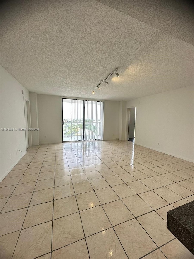 tiled empty room featuring rail lighting and a textured ceiling