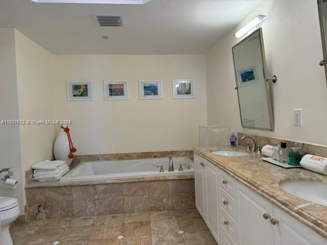 bathroom featuring tiled tub, toilet, and vanity