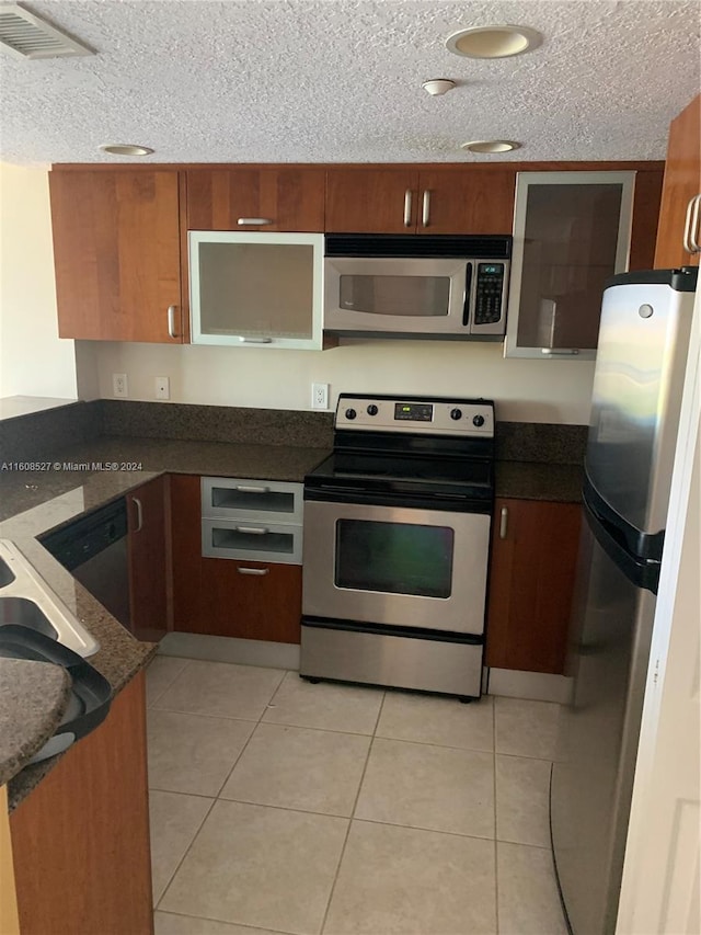 kitchen with light tile patterned flooring, appliances with stainless steel finishes, a textured ceiling, and kitchen peninsula