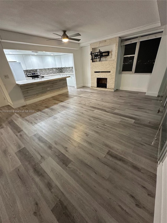 unfurnished living room with wood-type flooring, ornamental molding, ceiling fan, and a textured ceiling