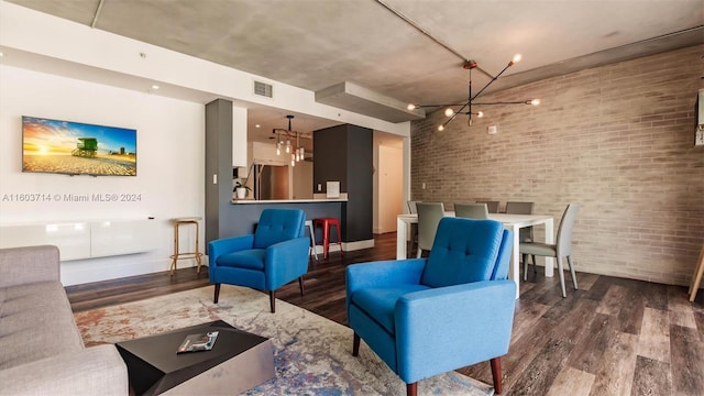 living room with hardwood / wood-style flooring, an inviting chandelier, and brick wall