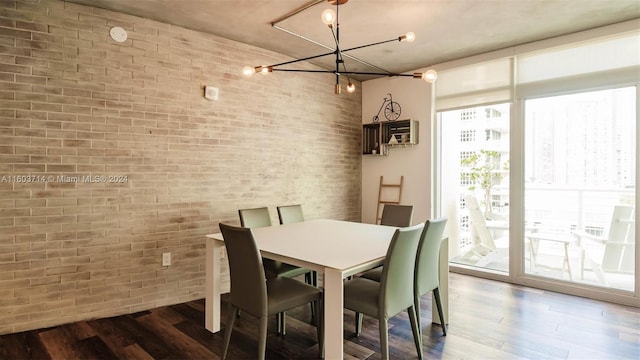 dining space featuring dark hardwood / wood-style floors, an inviting chandelier, and brick wall