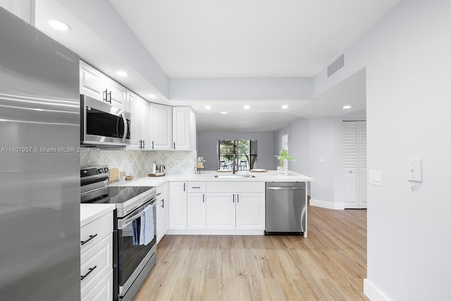 kitchen with white cabinets, sink, kitchen peninsula, stainless steel appliances, and light hardwood / wood-style floors