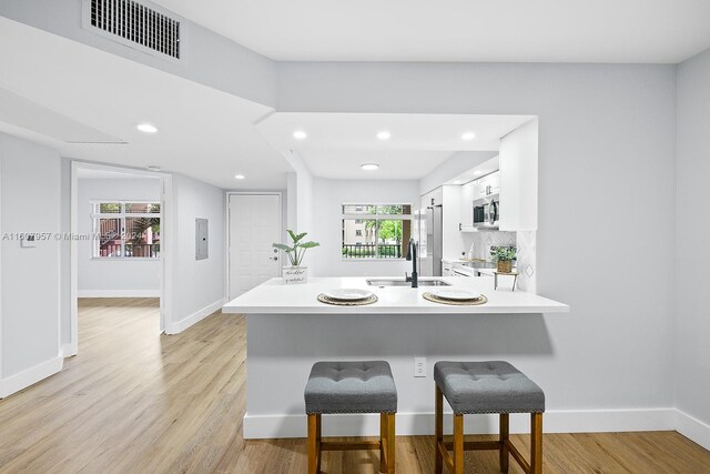 kitchen featuring light hardwood / wood-style flooring, white cabinetry, kitchen peninsula, and a kitchen breakfast bar