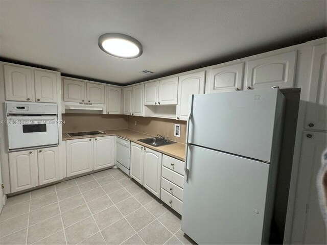 kitchen with light tile patterned floors, sink, white appliances, and white cabinets