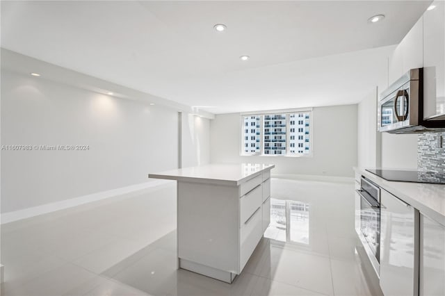 kitchen with a kitchen island, tasteful backsplash, white cabinets, light tile floors, and appliances with stainless steel finishes