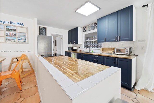 kitchen featuring sink, stainless steel appliances, tasteful backsplash, blue cabinets, and light tile patterned floors